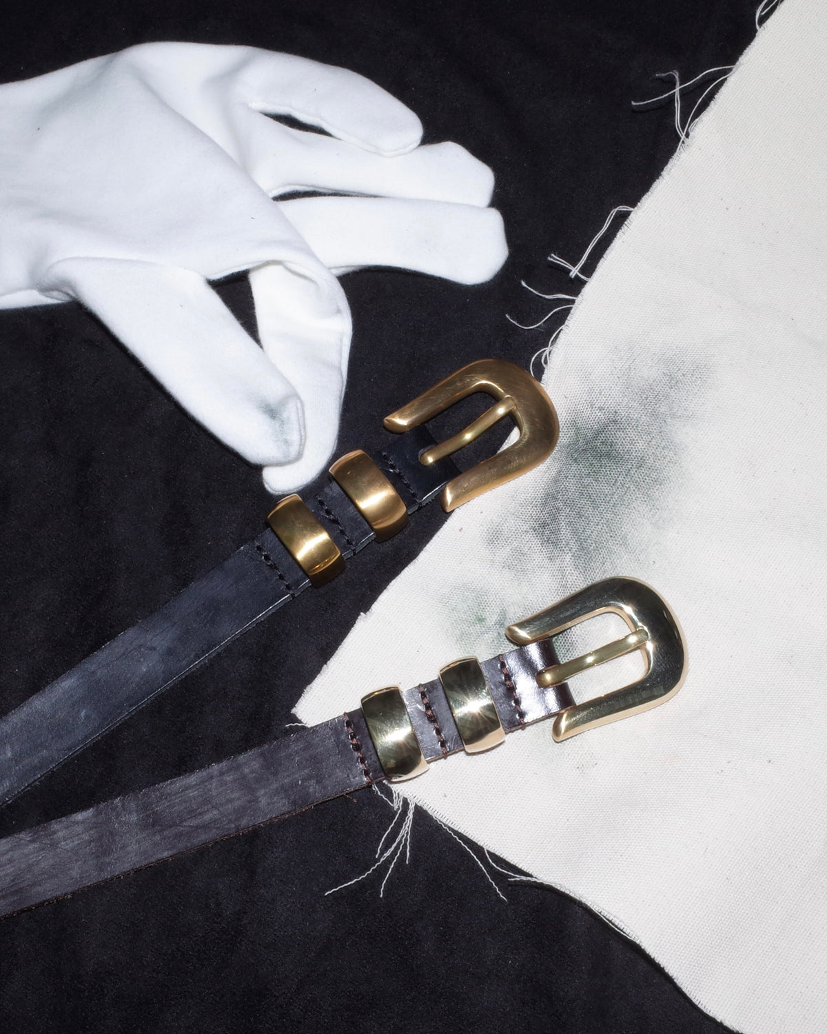 White-gloved handling of two JOEY belts, showing aged and freshly prepared unlacquered brass hardware.
