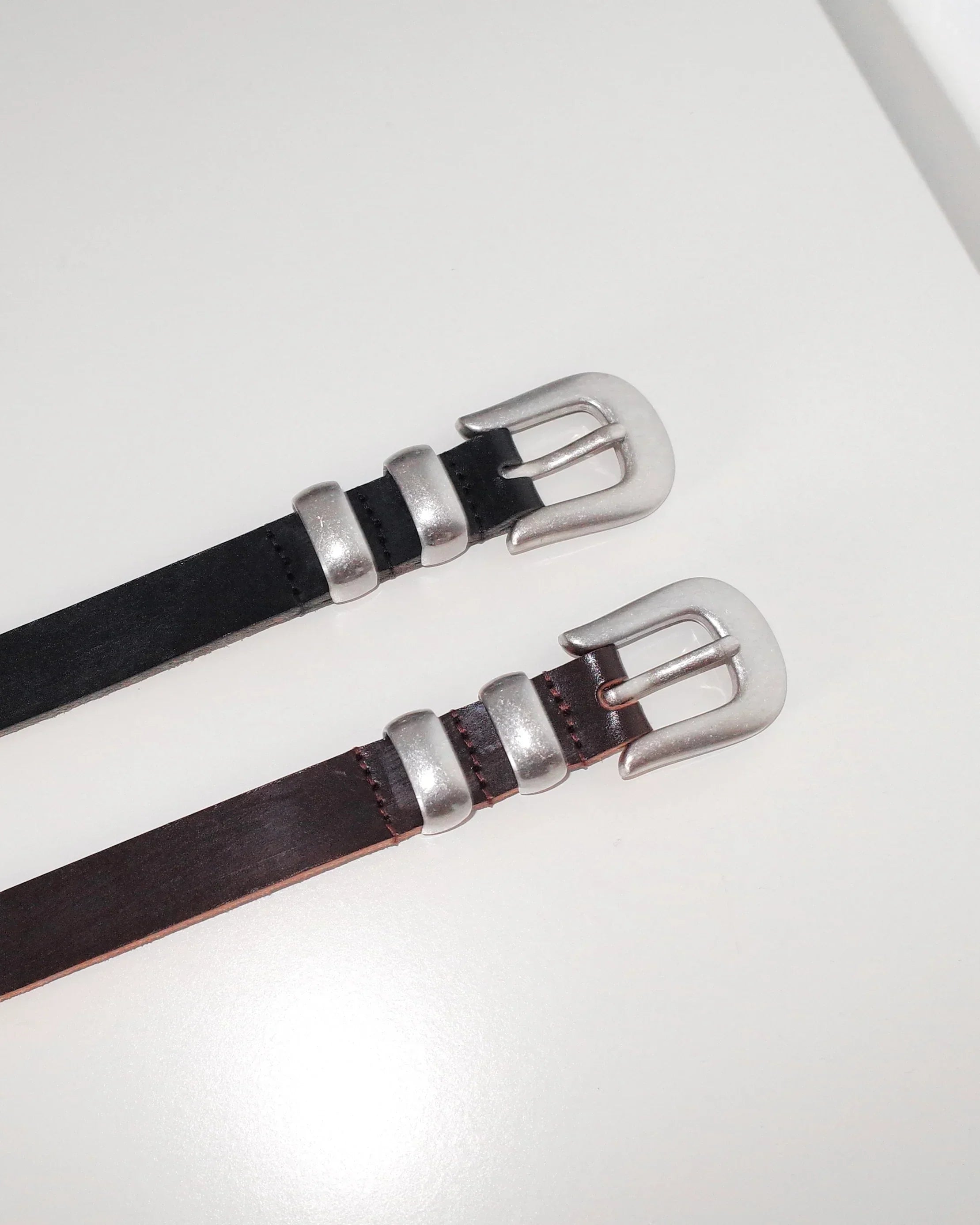Image of two stylish leather Western belt with metallic tips and buckles in black and brown, white background, product shoot