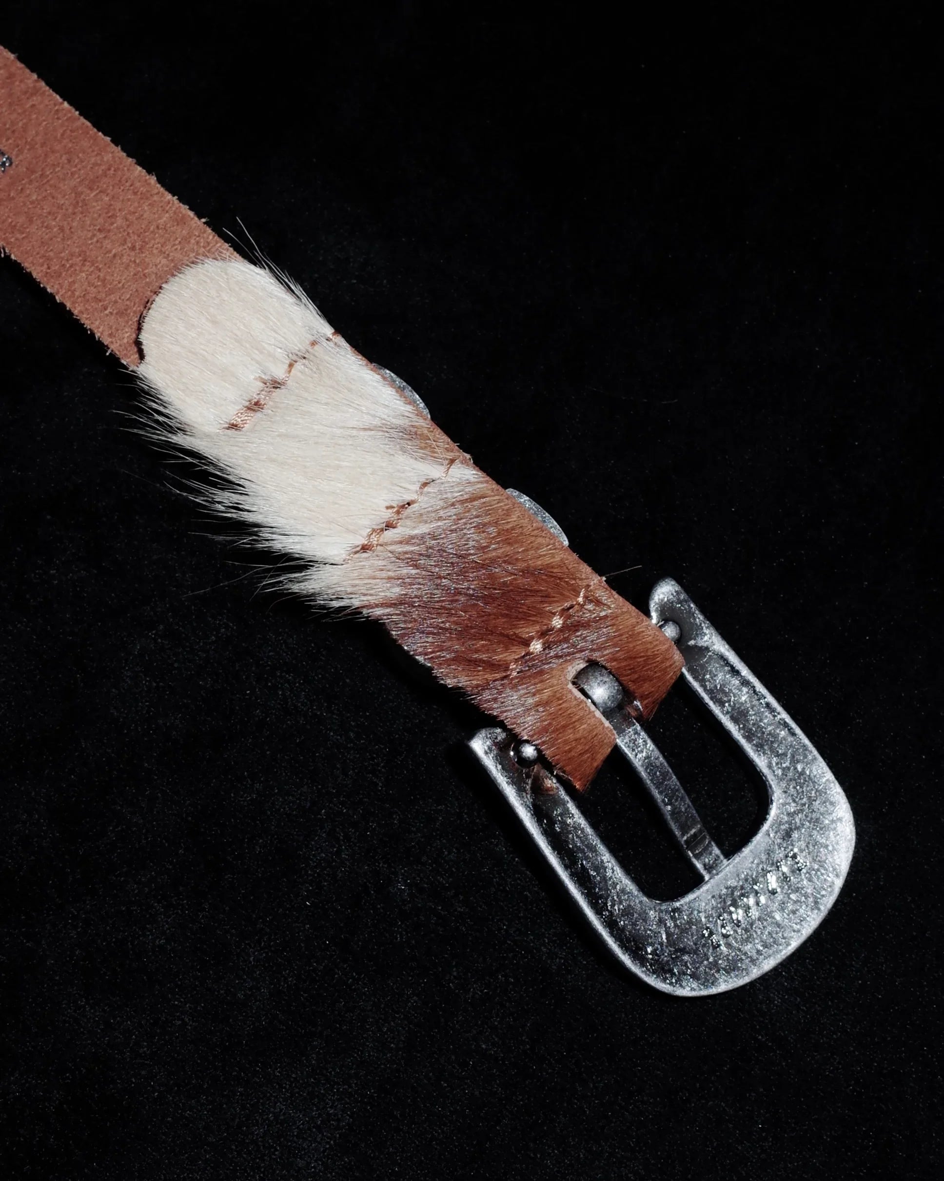 Brown leather belt with fur trim and silver buckle on a black background