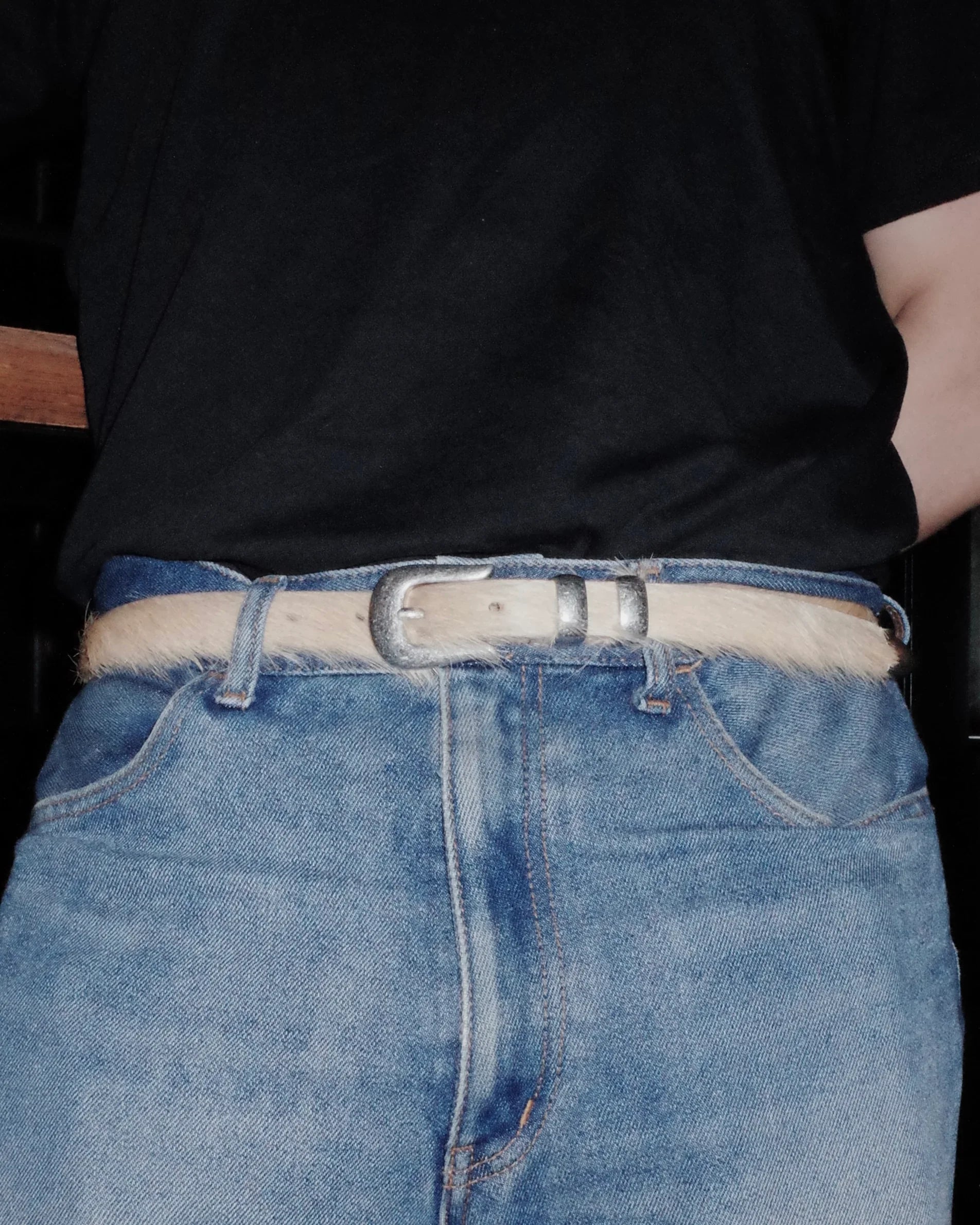 Person wearing blue jeans with a beige  Western belt and a black shirt.
