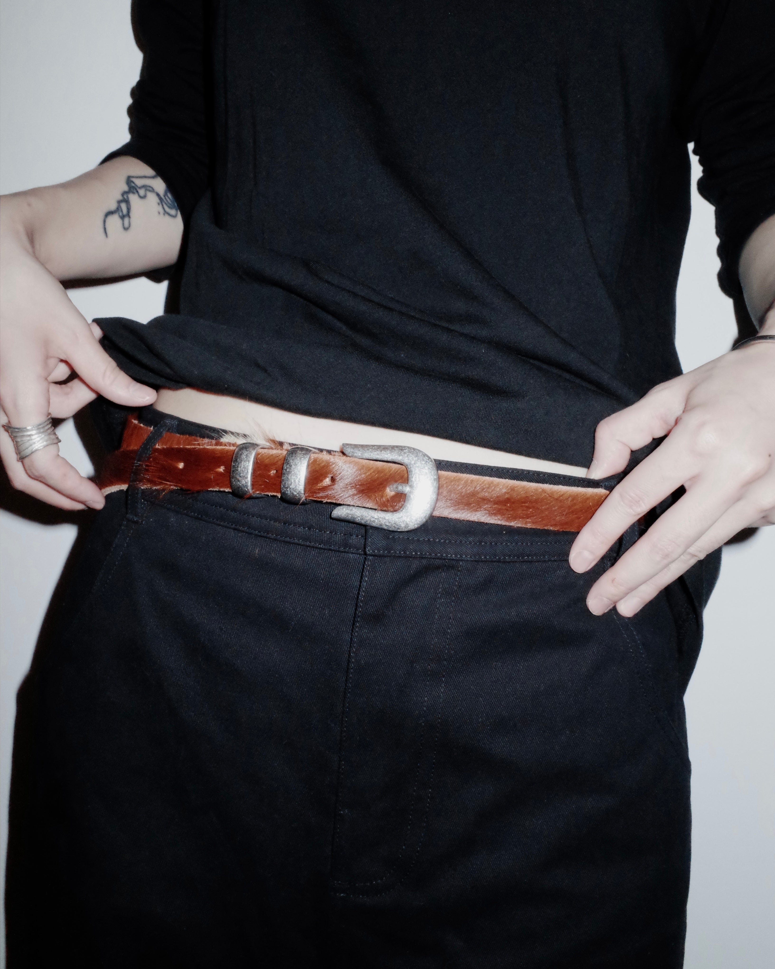 Person wearing a black shirt and dark pants with a brown Western belt.