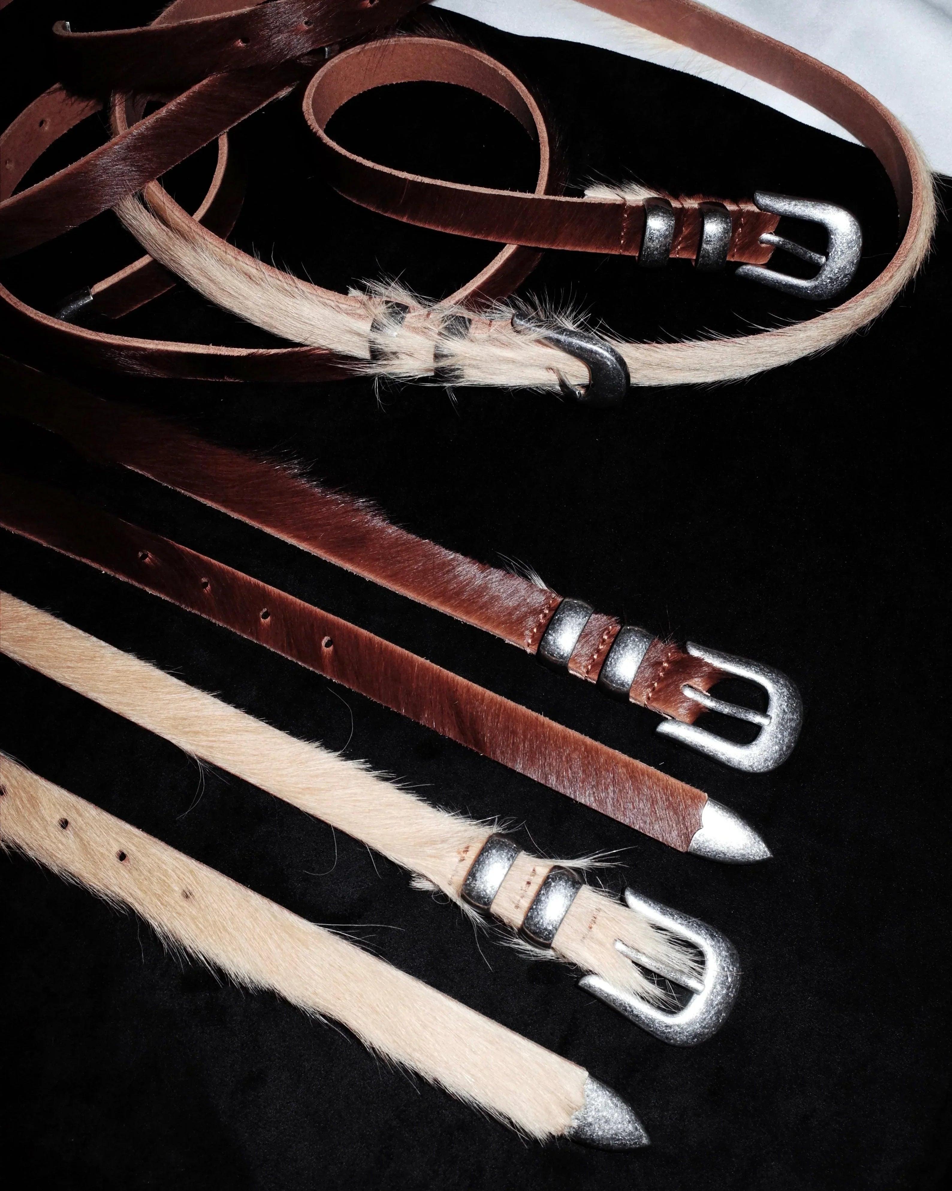 Set of leather Western belts with metal buckles on a dark surface