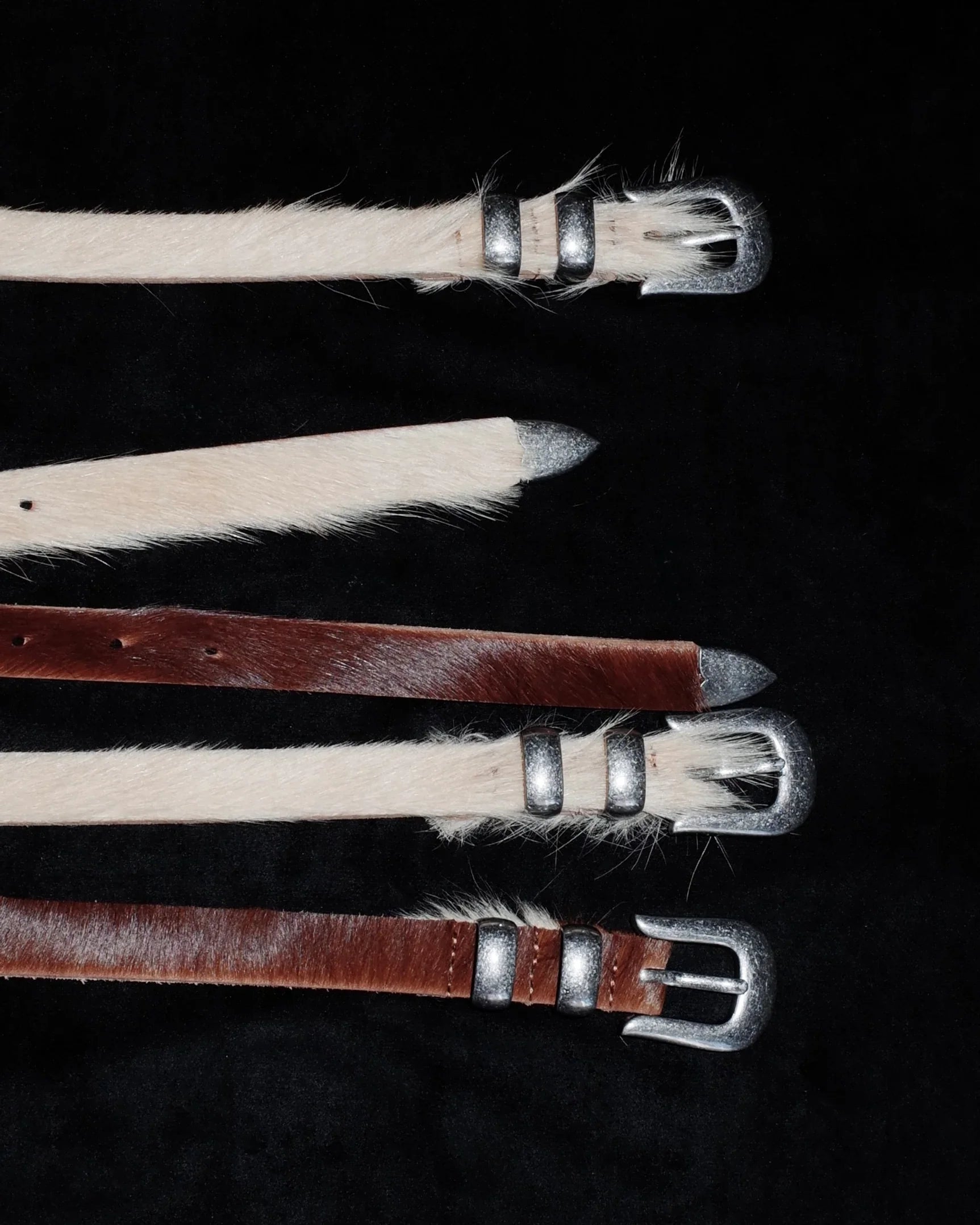 Three leather Western belt straps with metal buckles on a dark background