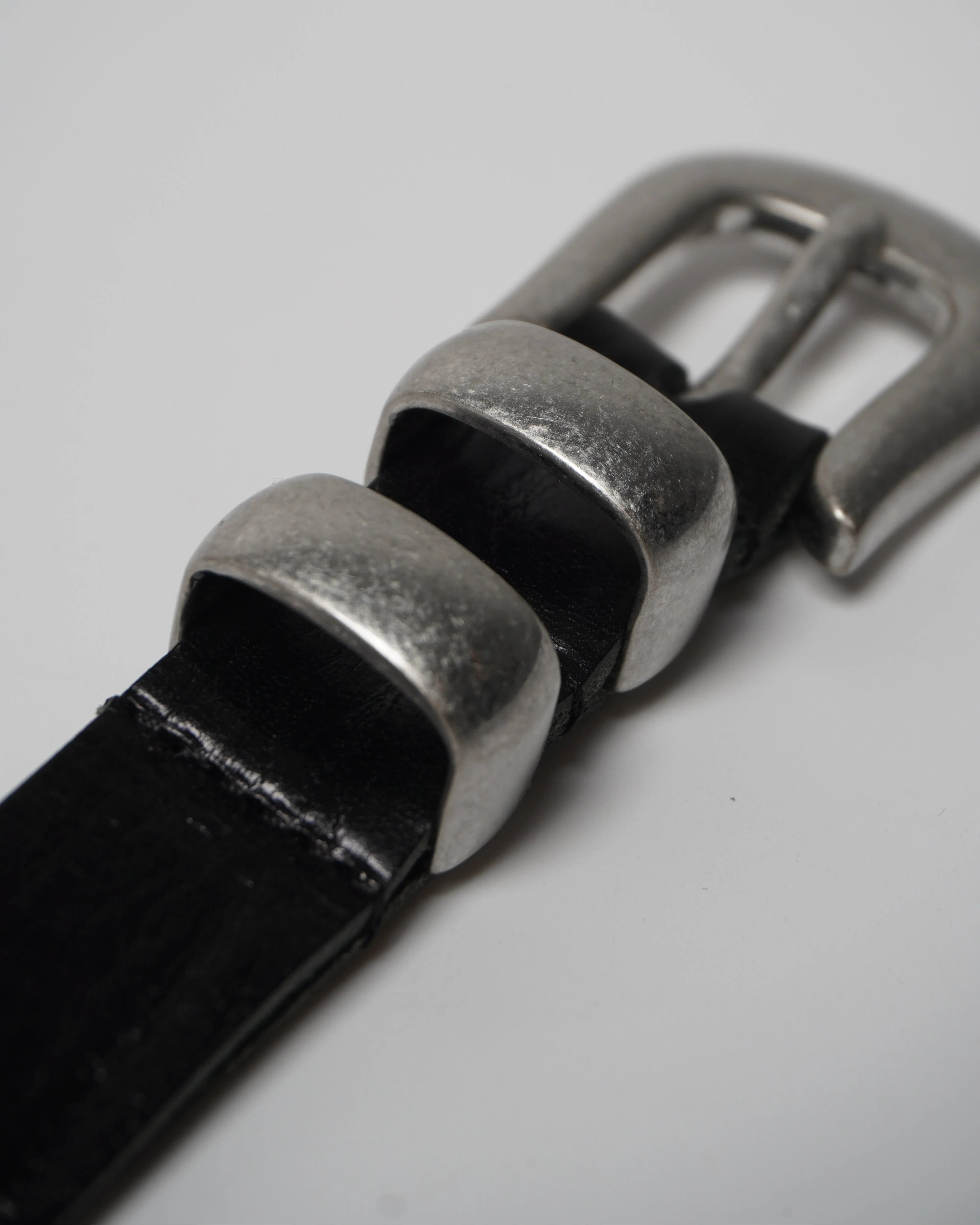 Image of a stylish black leather Western belt with metallic tips and buckles, placed on a white surface.