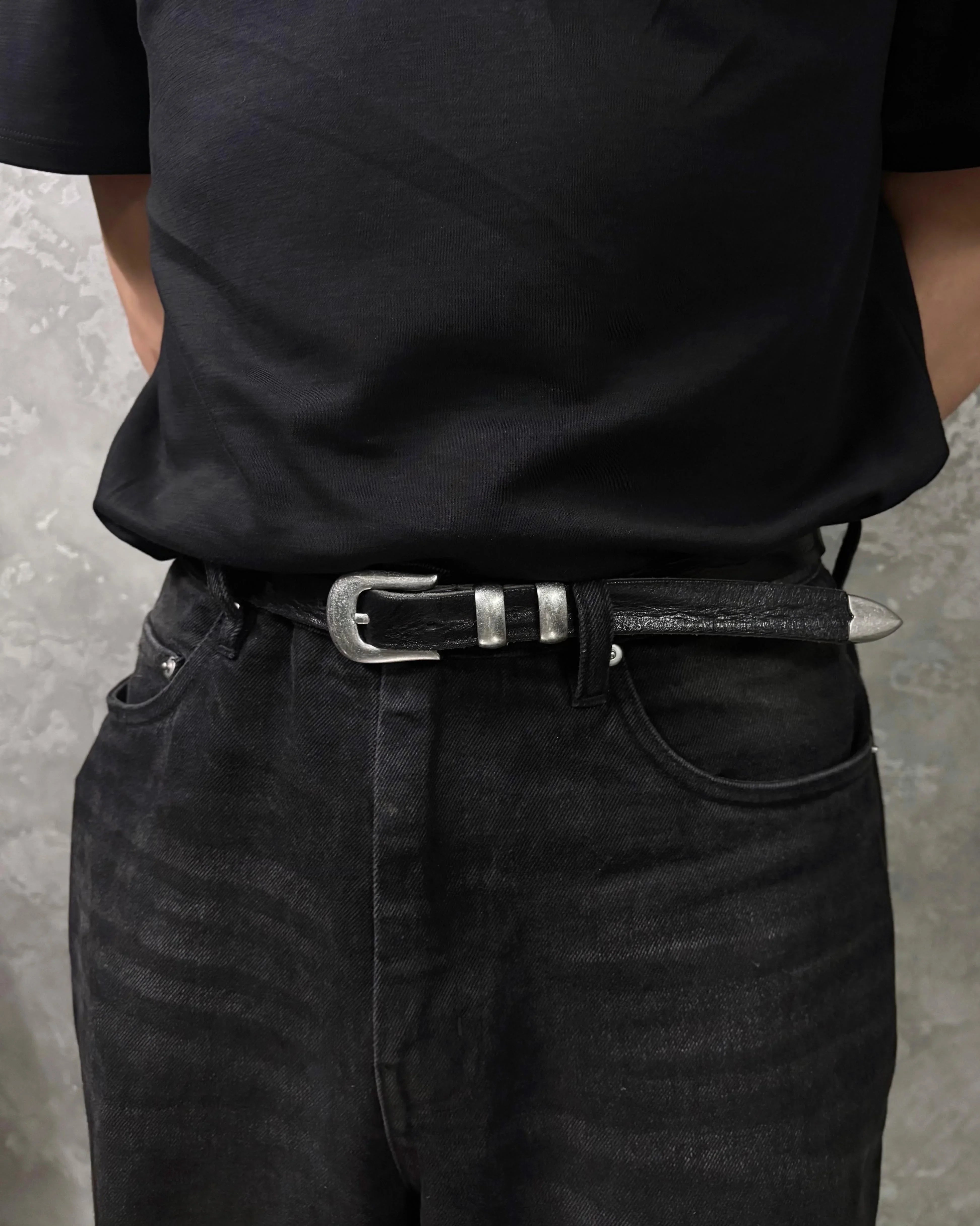 Image of a stylish black leather Western belt with metallic tips and buckles, pairing with black tee and a pair of black jeans.