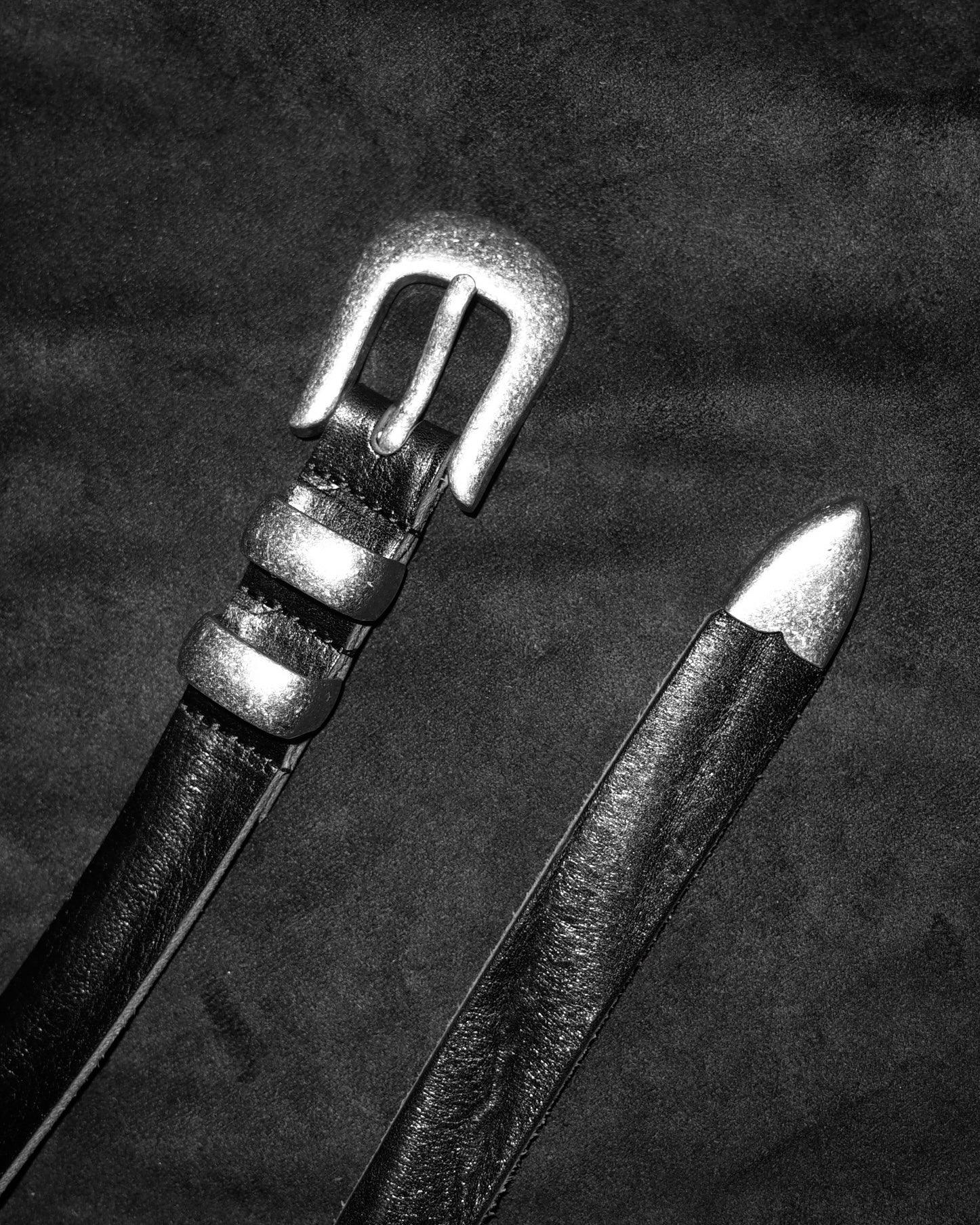 Image of a stylish black leather Western belt with metallic tips and buckles, placed on a dark fabric surface.