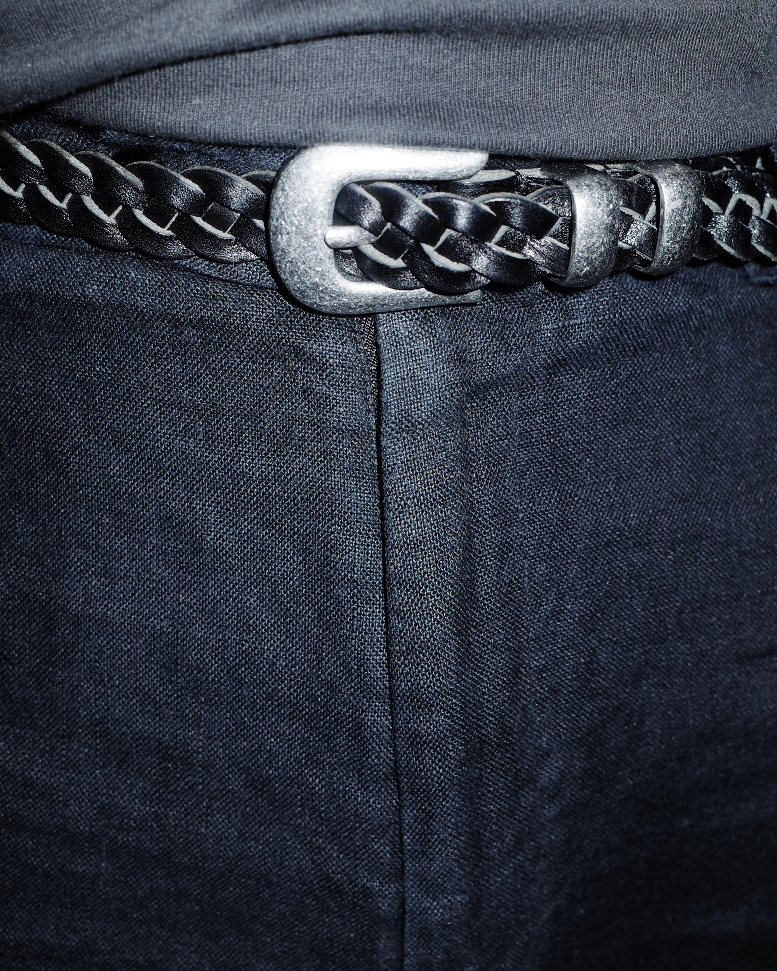Close-up of a black braided leather belt with a silver buckle pairing with linen trousers.