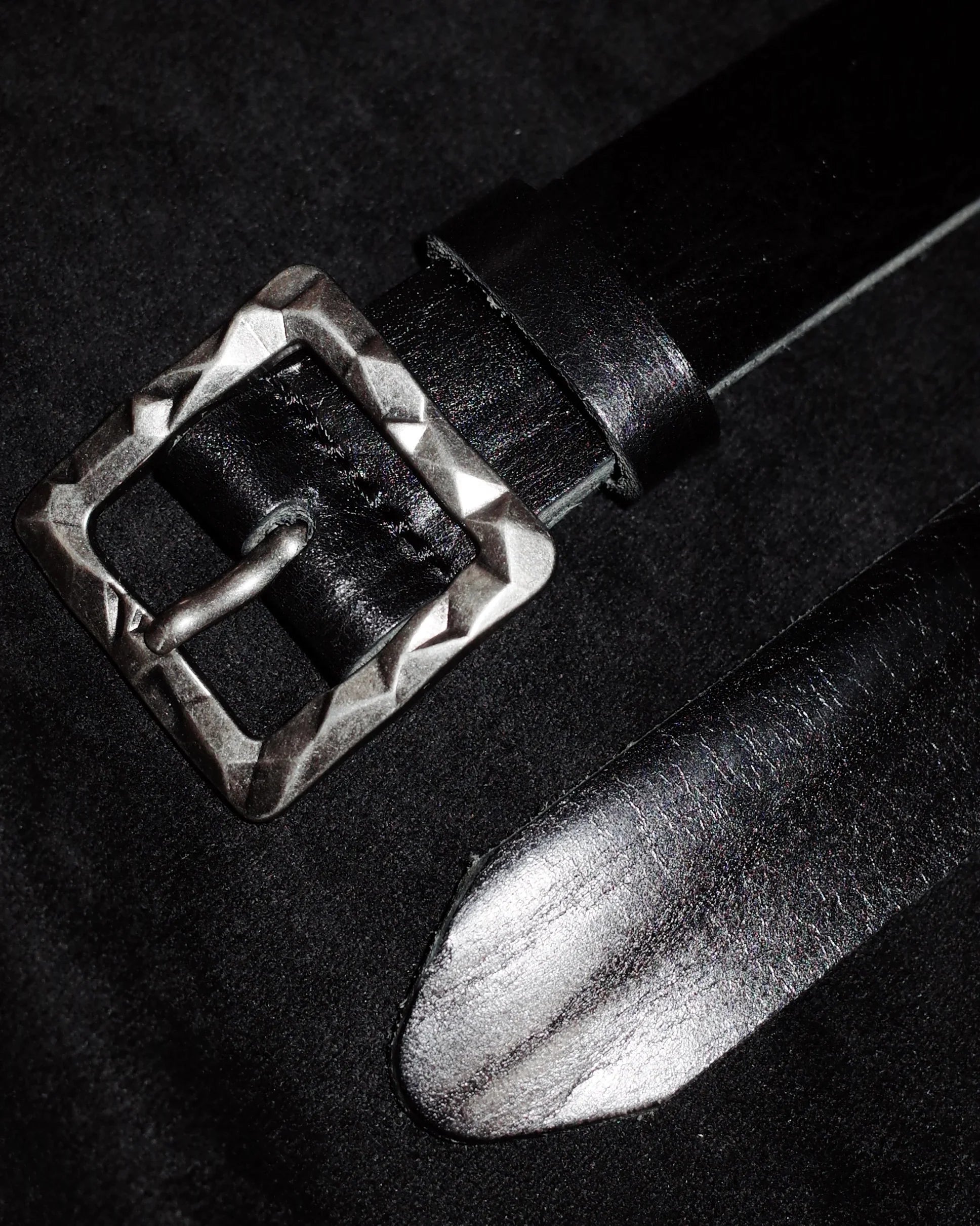 Black leather belt with a silver buckle on a dark background