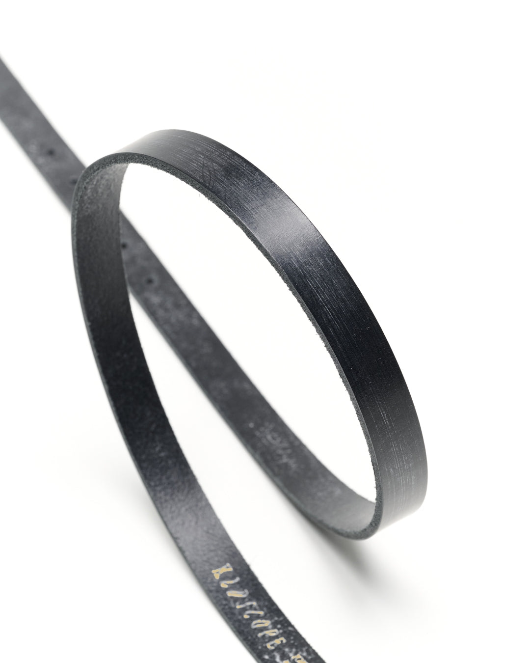 Curved strip of black Sedgwick bridle leather showing the slim 20mm profile and hand-finished edge of the JOEY belt.