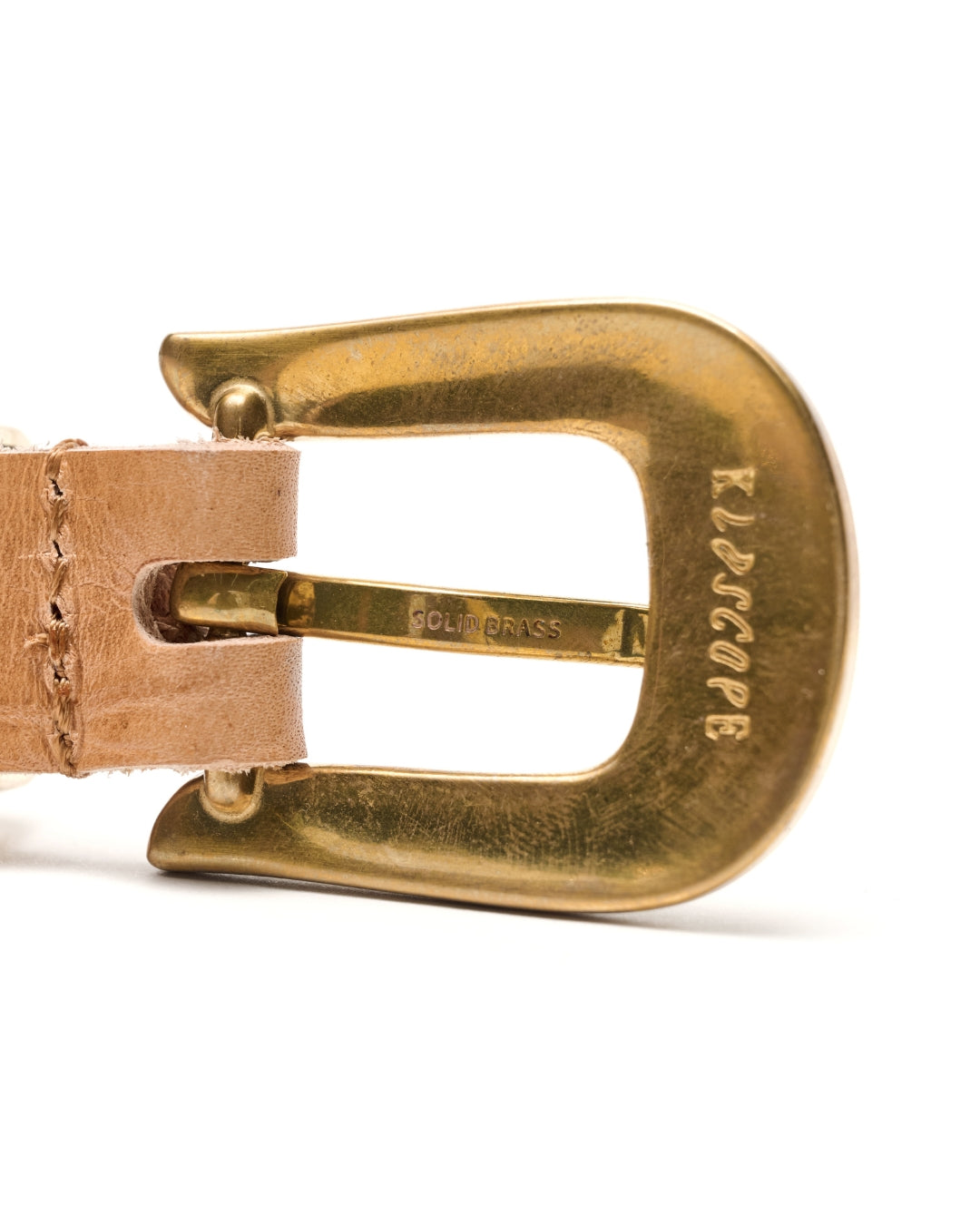 Close-up of a brass buckle with a tan leather strap, showing the brand name 'KLDSCOPE' engraved on the buckle, on a white background.