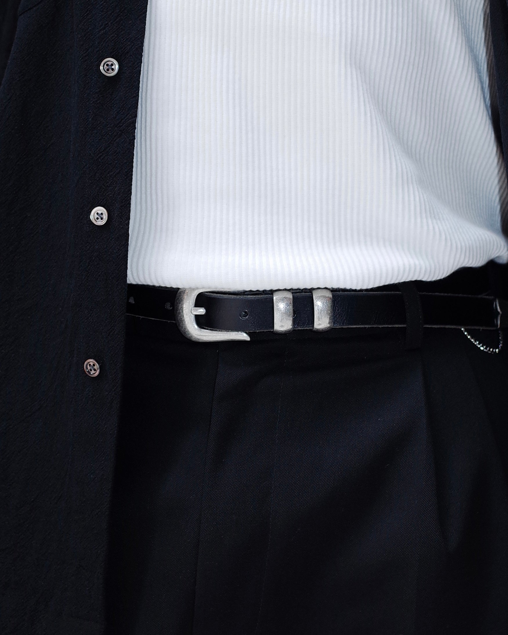 Close-up of a person wearing a black shirt, white ribbed sweater, and black pants with a western belt.