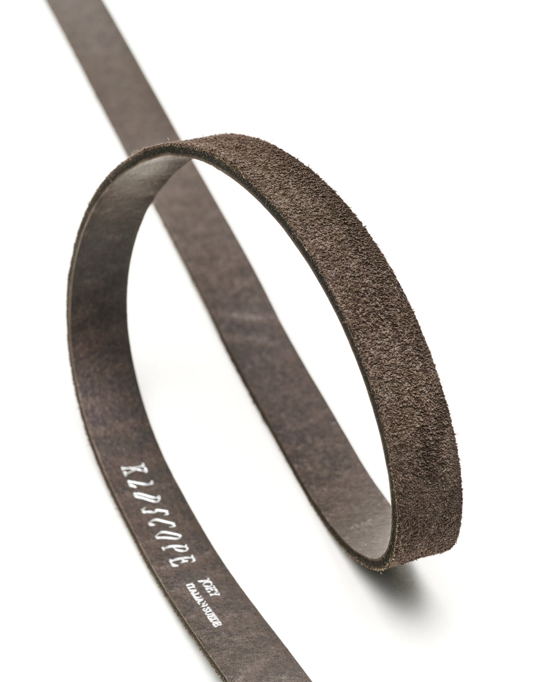 A charcoal-brown textured leather belt loop or strap, shown coiled on a clean white background. The inner band features silver printed branding text that reads 'KLDSCOPE'.