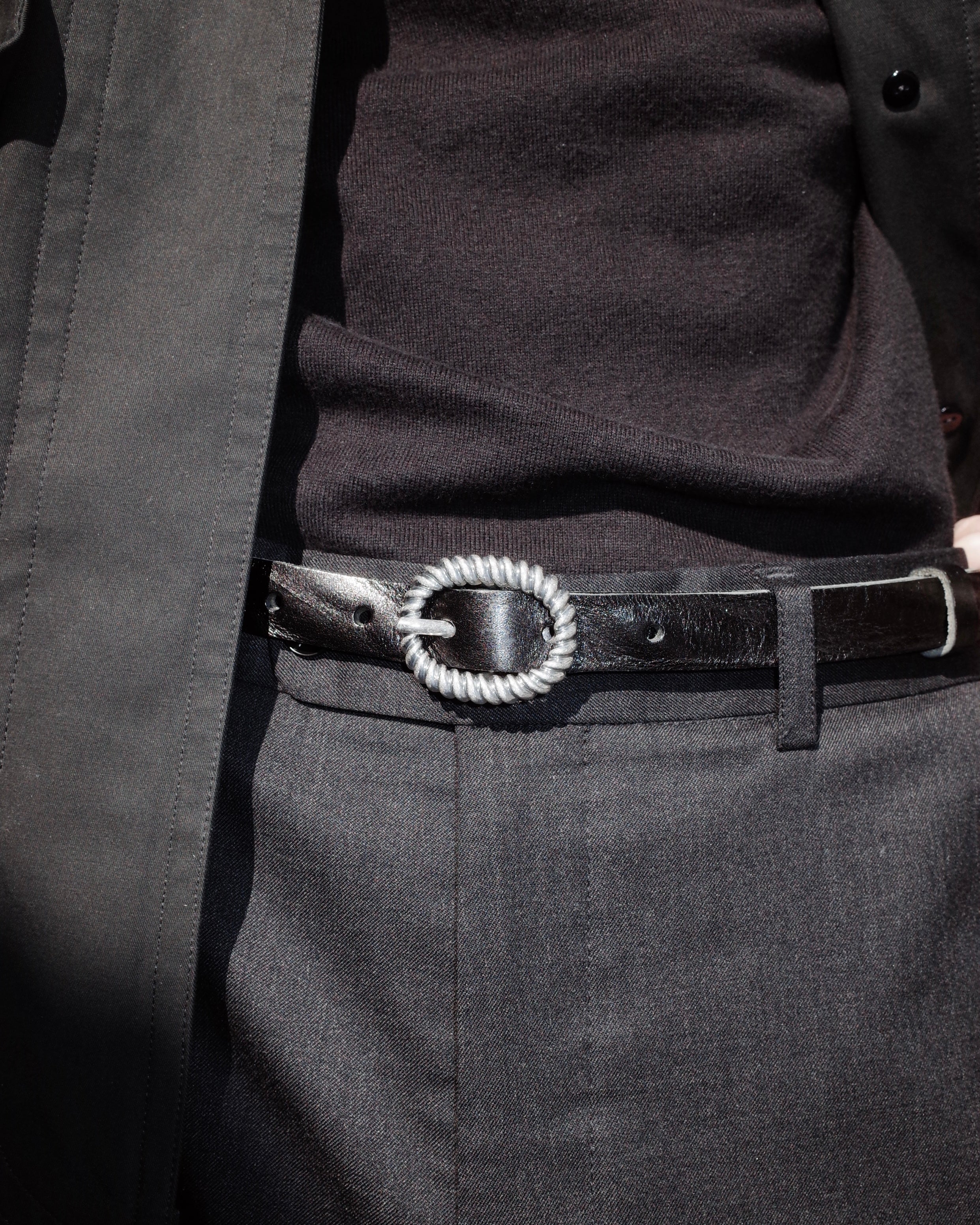 Close-up of a person wearing a black coat with a belt featuring a decorative buckle.