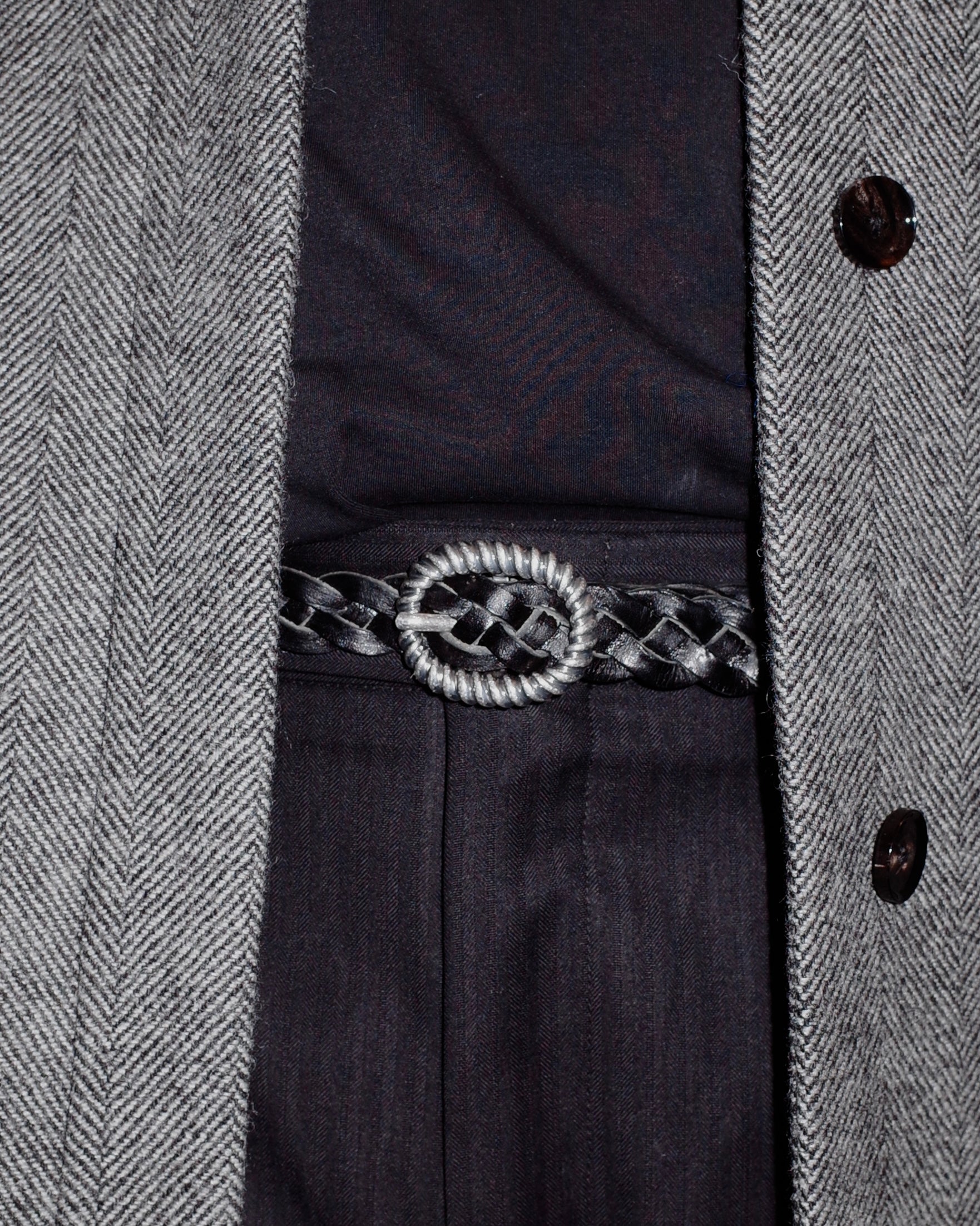 Close-up of a dark coat with a patterned belt and buttons.