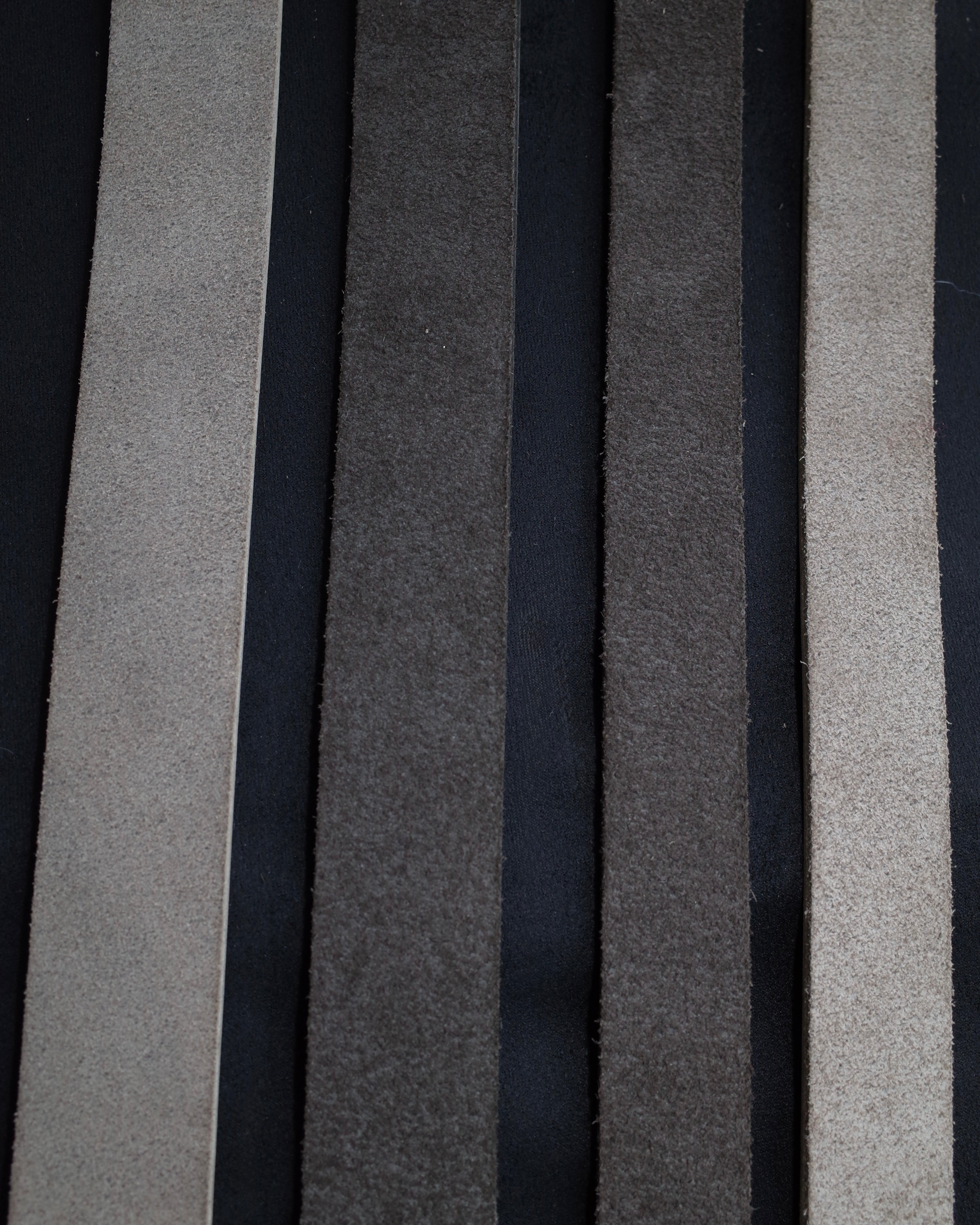 A close-up of vertical fabric or leather strips in multiple neutral colours, including black, charcoal grey, and sand grey arranged side by side.