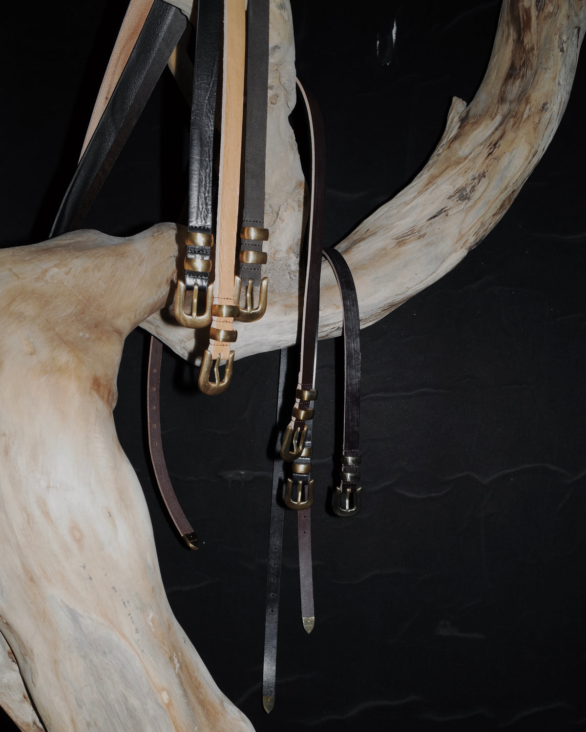 KLDSCOPE JOEY belts with unlacquered solid brass hardware displayed against sculptural wood.